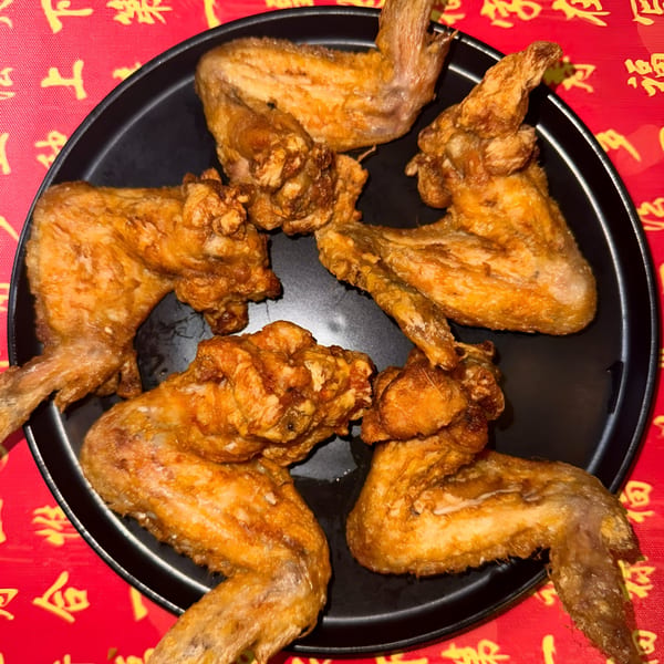 Crispy fried chicken wings on a black plate, set against a vibrant red and gold patterned tablecloth.